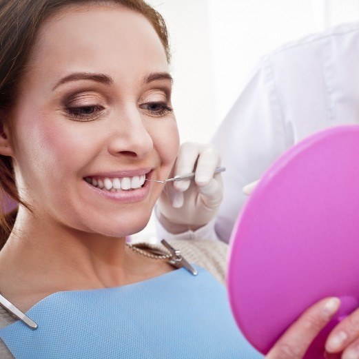 Dental patient looking in mirror at her new and improved smile