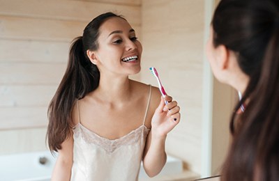 Woman smiling at reflection while brushing her teeth