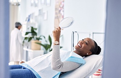 Woman smiling at reflection in handheld dental mirror