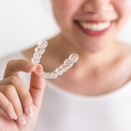Closeup of woman smiling while holding Invisalign aligner