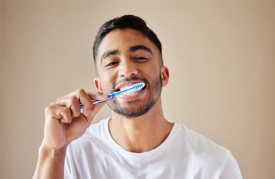 Man in white shirt smiling while brushing his teeth