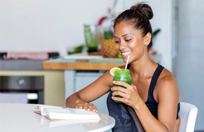 Smiling woman drinking green smoothie while reading