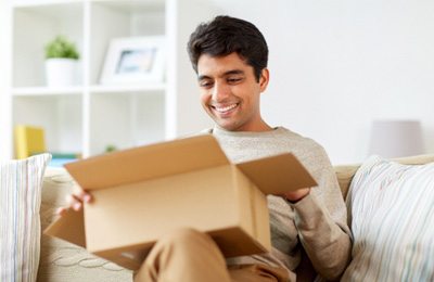 Man smiling while opening package on couch at home