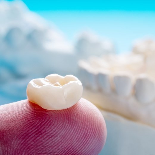 Person holding a dental crown on their finger